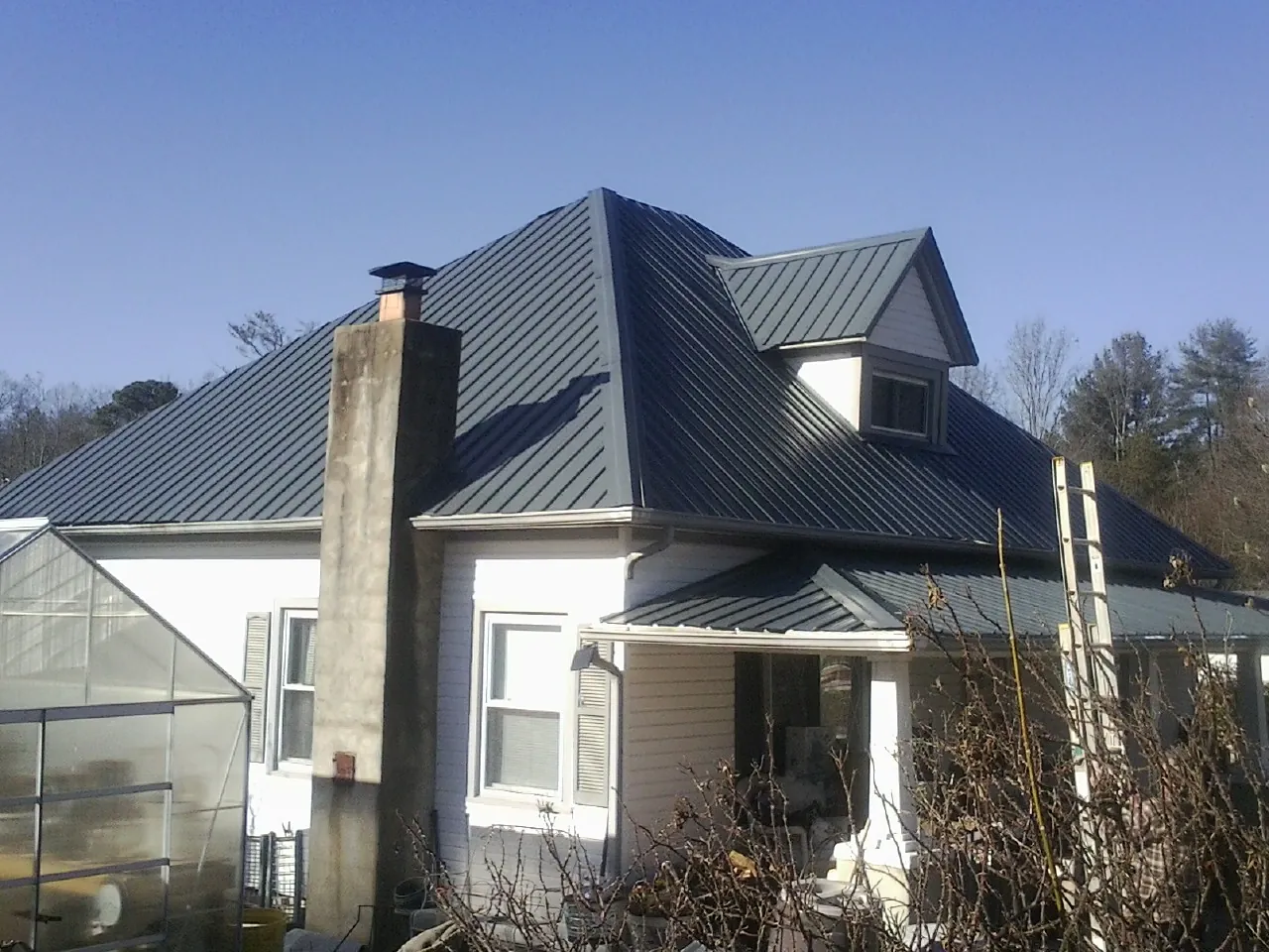 Dark blue standing seam metal roof on a white farmhouse with dormer — Slate & Tile Roof Repair by Roofing Brothers in Marion Center
