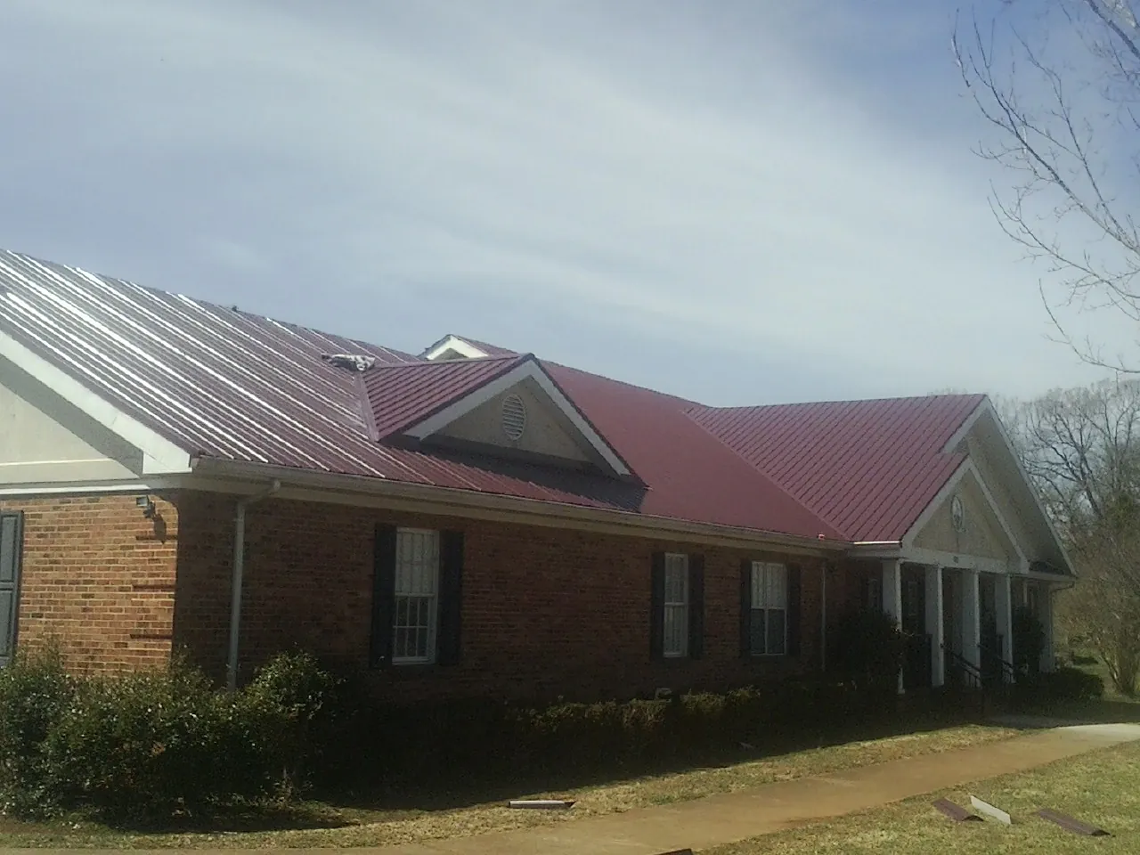 Red metal roof with gabled entries on a long brick building, from a Hail Damage Roof Repair job in Marion Center