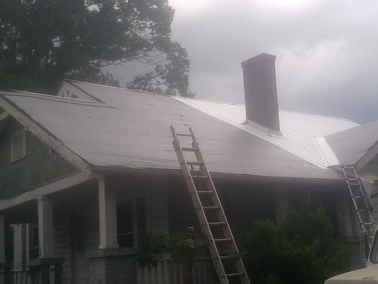 Ladders against a metal roof on an older home with a brick chimney in Marion Center