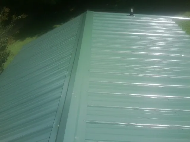 New green metal panels meeting at the ridge of a roof — Flat Roof Repair work by our crew in Marion Center