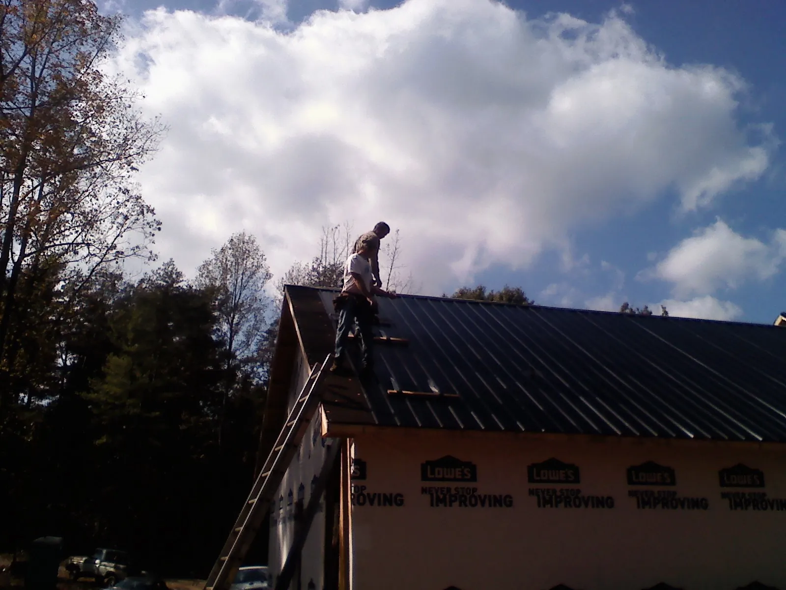 Roofer fastening dark metal panels high against a cloudy sky, from a Roof Inspection job in Marion Center