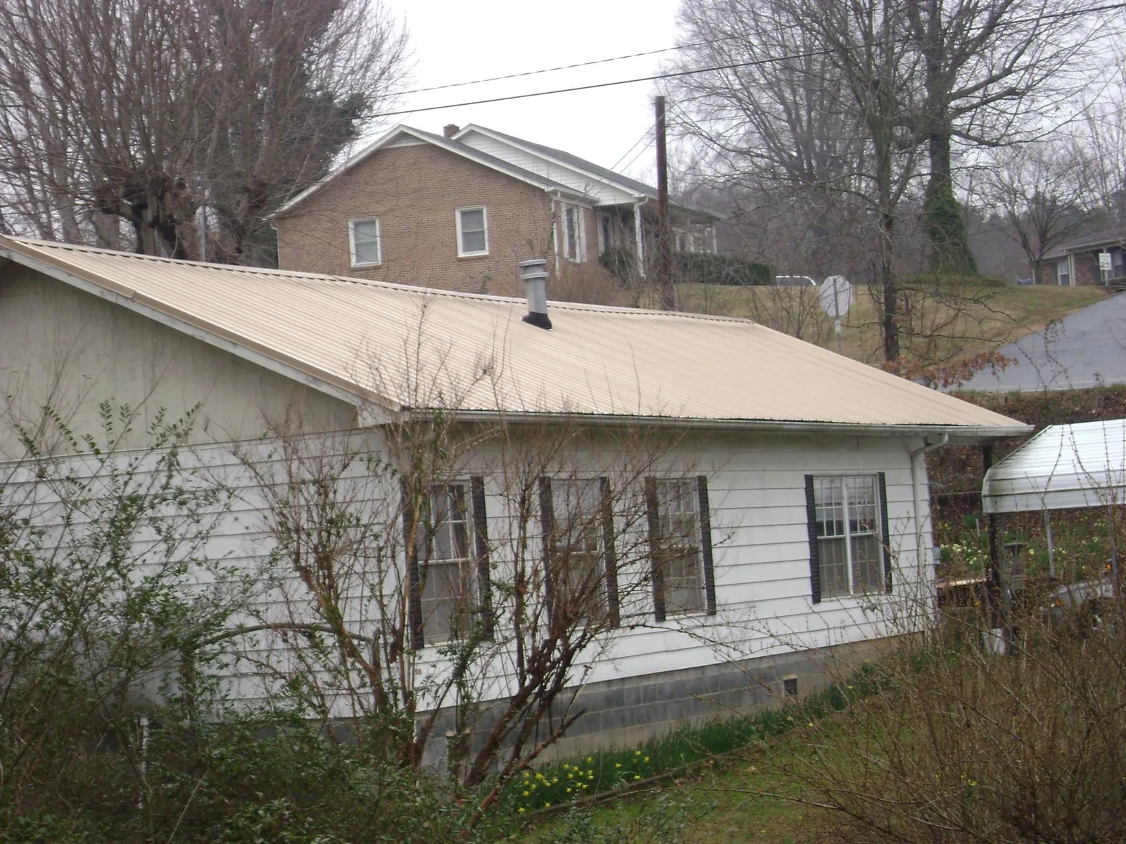 Tan metal roof on a white sided house set into a hillside — Commercial Roofing by Roofing Brothers in Marion Center