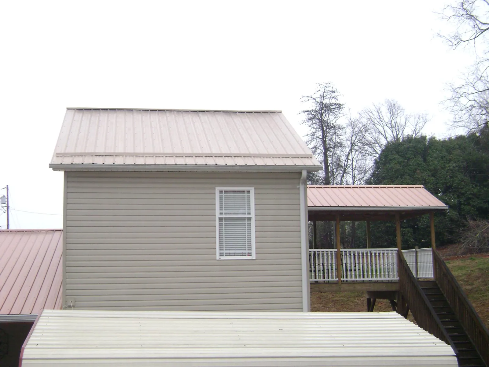 Tan metal roofs on a two story addition and attached porch, from a Roof Replacement job in Marion Center